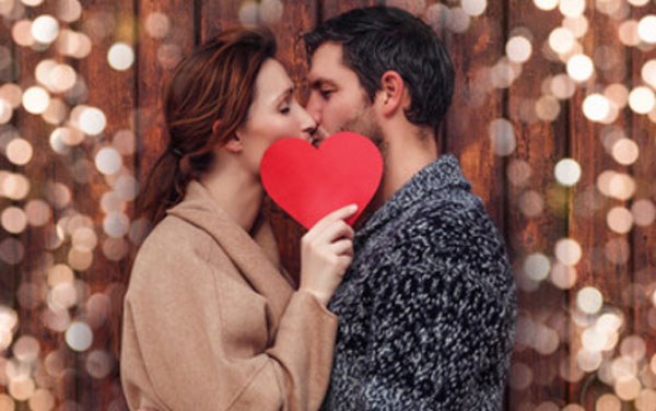 Парень с девушкой целуются. Она прикрывает их картонным сердечком