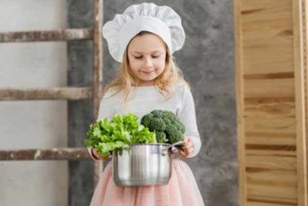 Девочка с колпаком на голове несет кастрюлю с овощами