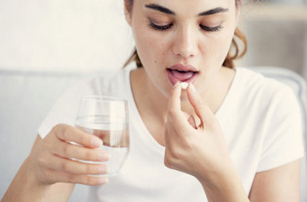 Женщина кладет в рот таблетку. Собирается запивать ее водой