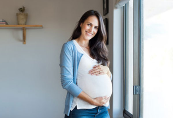 Беременная женщина держится за свой живот и улыбается