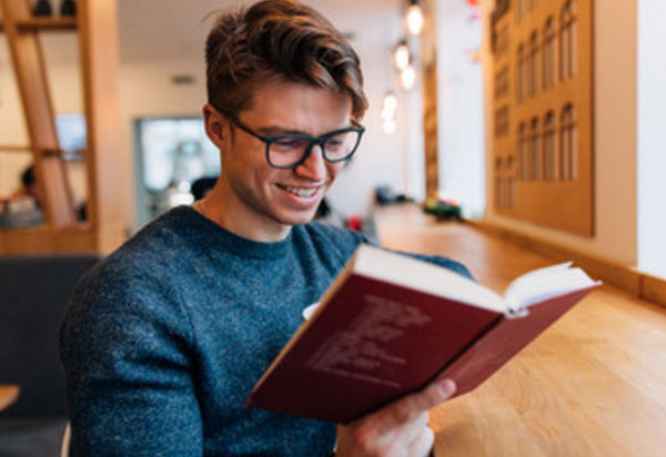 Улыбающийся мужчина в очках читает книгу