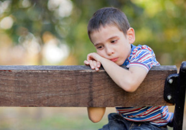 Одинокий грустный мальчик сидит на скамейке