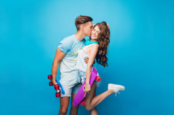 Парень целует девушку в щечку. У обоих в руках скейты