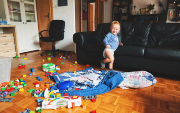 Маленький мальчик стоит посреди комнаты, в которой разбросаны игрушки