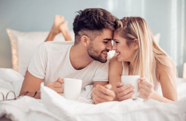 Мужчина с женщиной лежат на кровати, тулятся носами друг к другу