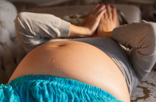 Беременная женщина лежит на кровати, прячет лицо руками