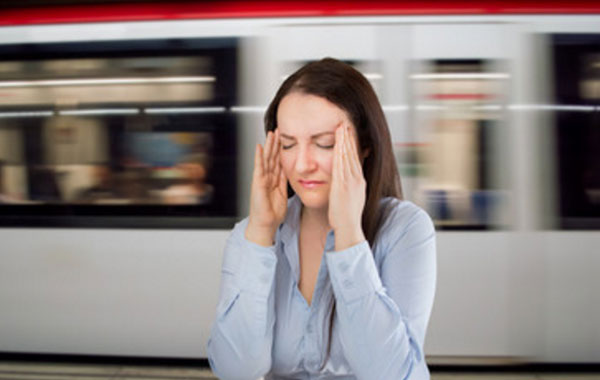 Женщина держит пальцы на висках. Сзади проносится вагон поезда в метро