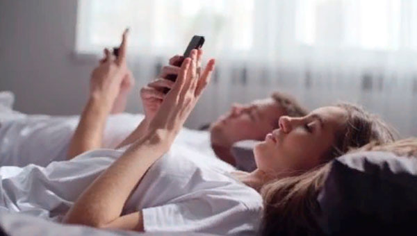 Мужчина и женщина лежат в кровати и смотрят в свои телефоны