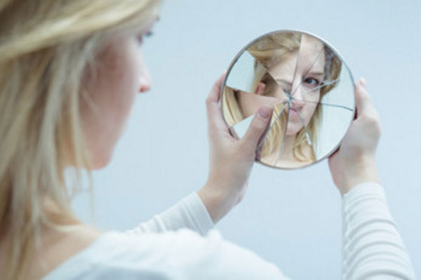 Девушка с комплексами смотрит на свое отражение в разбитом зеркальце