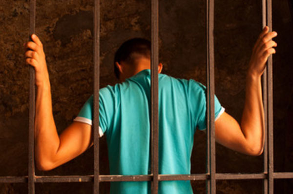 Мужчина стоит спиной, прижимается к тюремной решетке