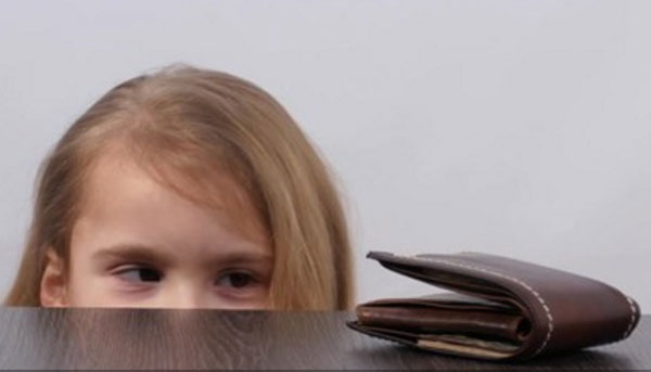 Девочка заинтересовано смотрит на кошелек, который лежит на столе