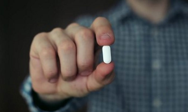 Мужчина пальцами удерживает белую таблетку овальной формы