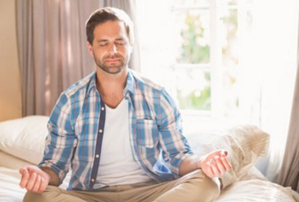 Спокойный мужчина сидит в позе йога на диване
