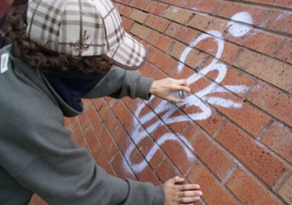 Ребенок в кепке и завязанным лицом рисует граффити на стене