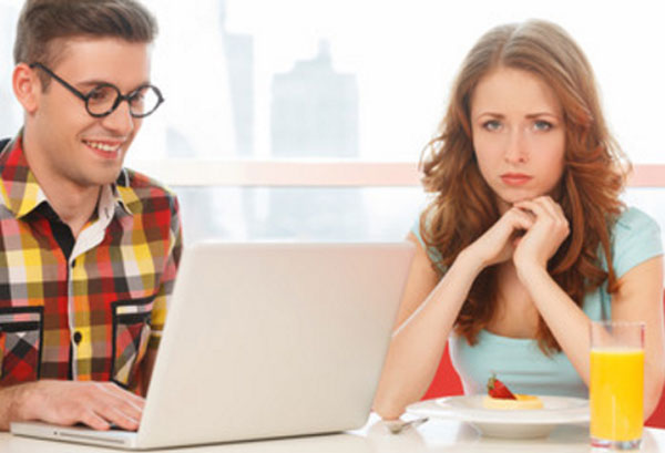 Расстроенная девушка сидит рядом с мужчиной в очках, который увлечен своим ноутбуком