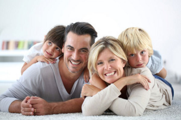 Счастливая семья из родителей и двух деток. Лежат на ковре и улыбаются