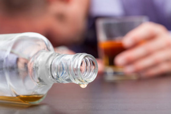 Пустая бутылка алкоголя, на заднем плане парень со стаканом, лежит лицом на столе
