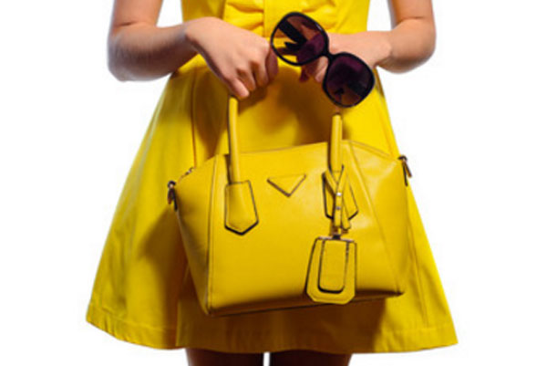 Девушка в желтом платье с желтой сумочкой и солнцезащитными очками в руке
