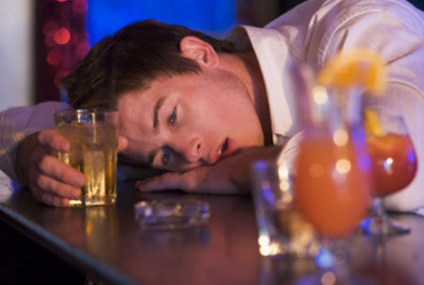 Пьяный мужчина с стаканом алкоголя в руках лежит на стойке бара