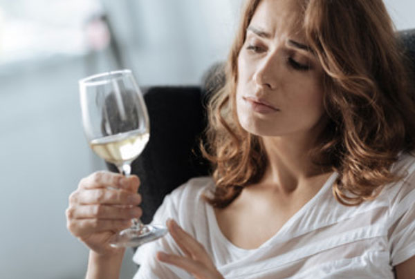 Женщина держит в руке бокал вина. Грустно на него смотрит