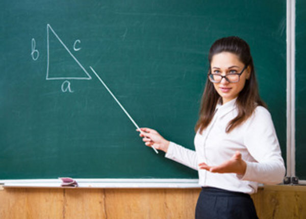 Строгая учительница в очках стоит возле доски с указкой в руке