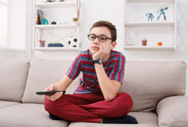 Мальчик в очках с пультом в руках сидит на диване