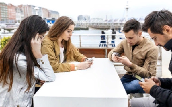 Компания людей сидит за одним столом и все смотрят в свои телефоны