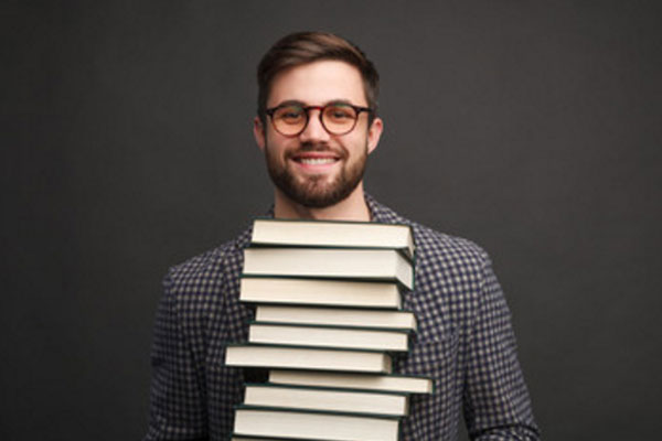 Улыбающийся парень в очках с стопкой книг в руках