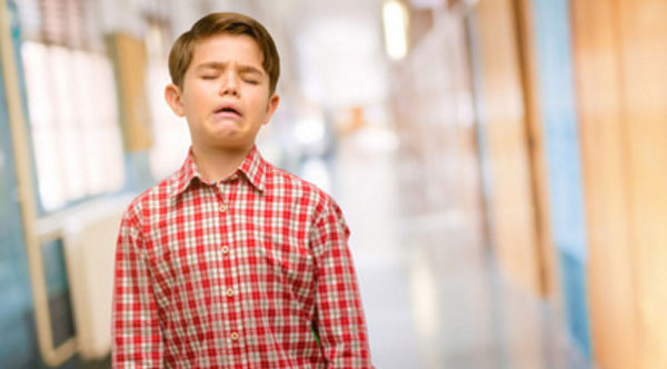 Мальчик стоит посреди школьного коридора. Начинает плакать