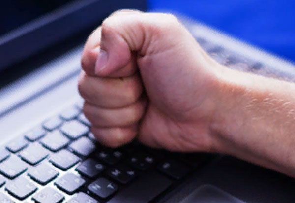 Мужчина бьет кулаком по клавиатуре ноутбука