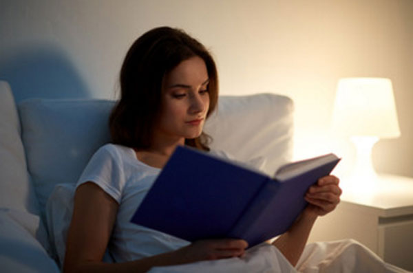Женщина читает, сидя в кровати при включенном ночнике