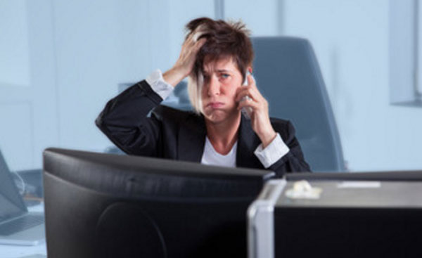 Замученная женщина говорит по телефону, сидя на работе за столом, перед компьютером