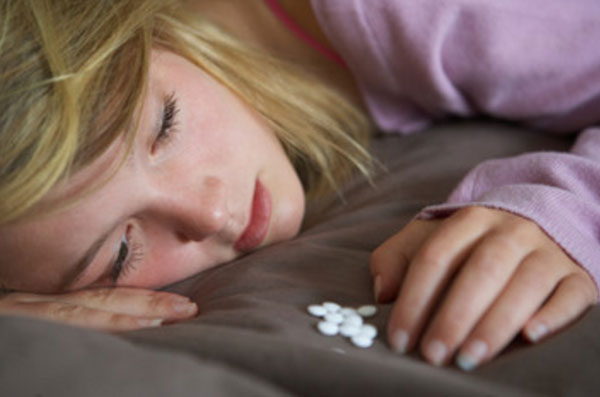 Девушка лежит на кровати и смотрит на горстку таблеток