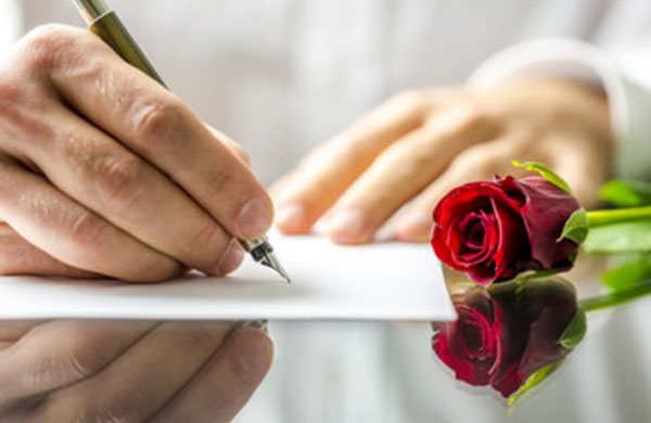Мужчина пишет письмо. Рядом на столе красная роза
