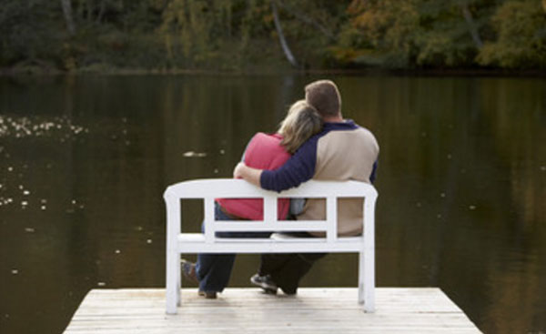 Влюбленная пара сидит на скамейке, на мостике, перед рекой