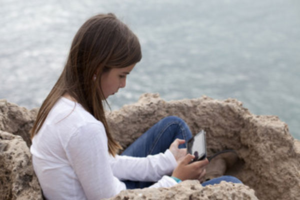 Девочка сидит на возвышенности возле моря с мобильником в руках